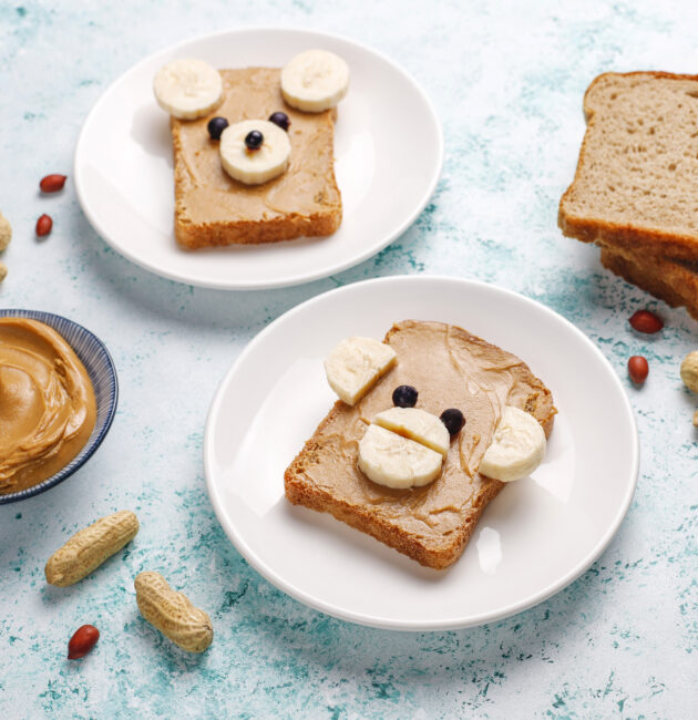 Funny bear and monkey face sandwich with peanut butter, banana and black currant on light background,top view