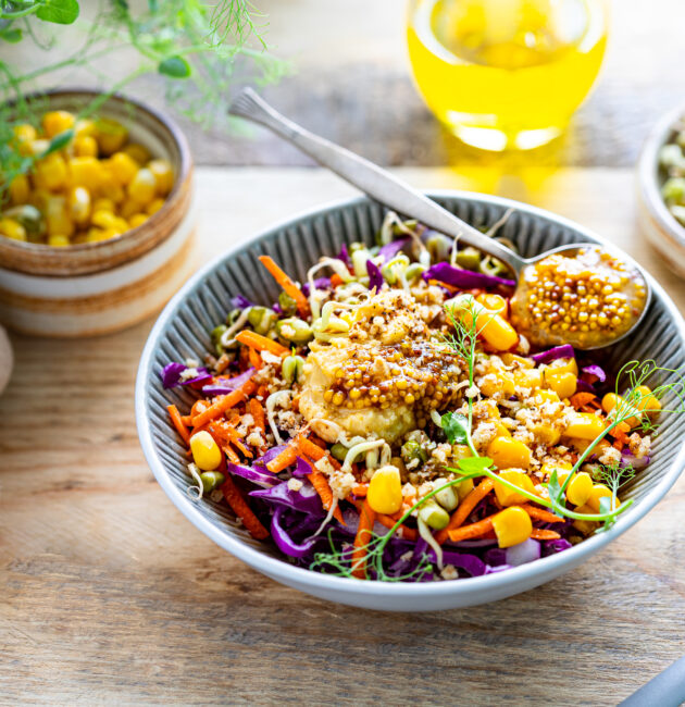 Vegetable salad of fresh red cabbage with carrots, onions, corn, mung seedlings in a plate on wooden background. Selective focus.